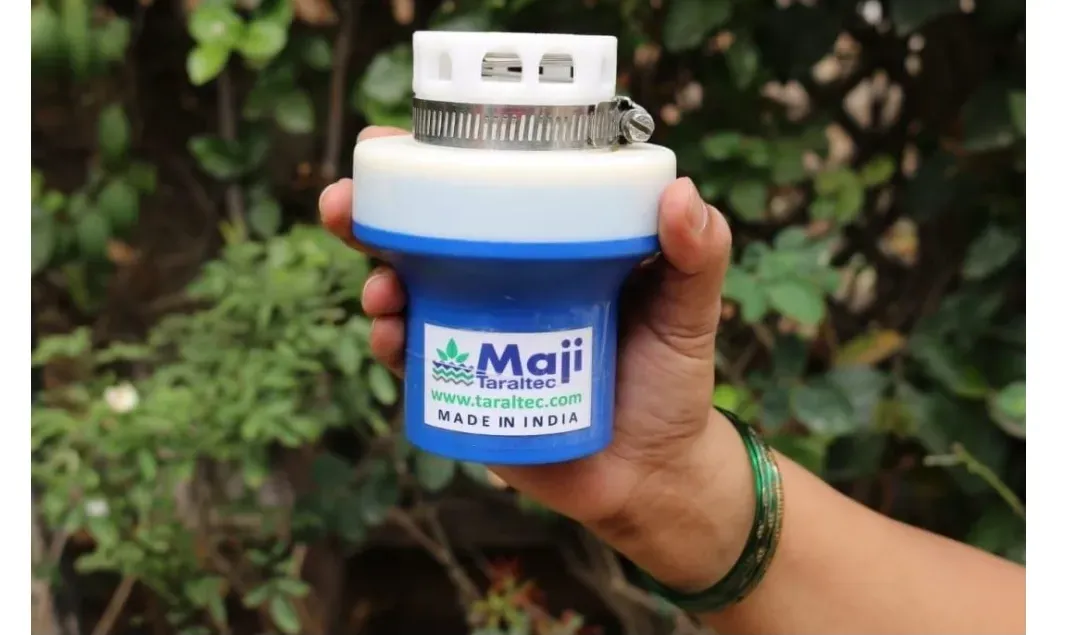 A hand holds the palm-fitting Maji:Taraltec® Reactor, a cylindrical device with a blue tapering base and metal cap, against green foliage.