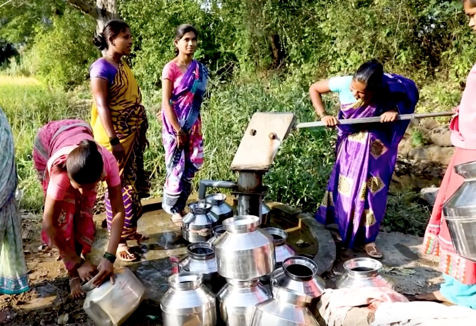 Women in a village in India draw drinking water from an India Mark II hand pump, filling steel pots.